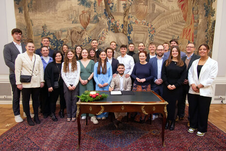 Gruppenbild: Die Damen- und die Herrenmannschaft der Bonn Capitals mit Oberbürgermeisterin Katja Dörner im Gobelinsaal, um einen Tisch herum stehend.