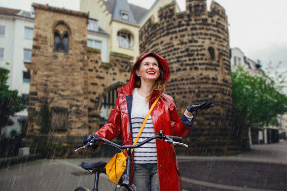 A young woman with a bicycle stands in the rain