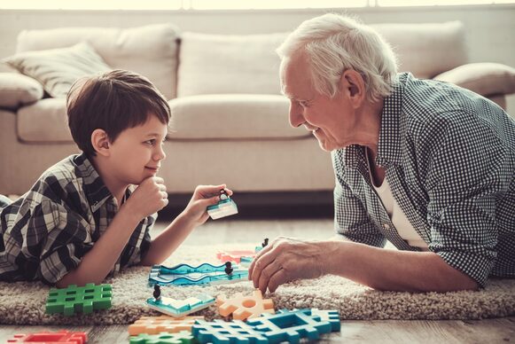 Ein Senior und ein Junge liegen auf einem Teppich und spielen.