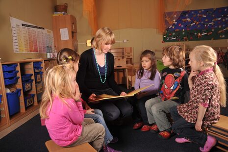 Une femme lit un livre aux filles de l'école maternelle