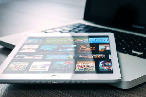 iPad лежит на Macbook. На iPad изображены предложения потоковой платформы.
