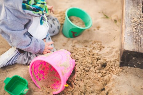 Un enfant à genoux dans un bac à sable, entouré de seaux et de moules.