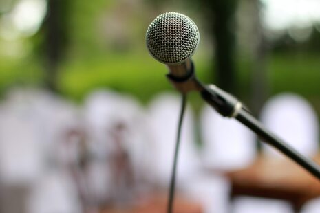 Ein Mikrophon auf einer Open Air-Bühne, im Hintergrund ist verschwommen Publikum zu sehen