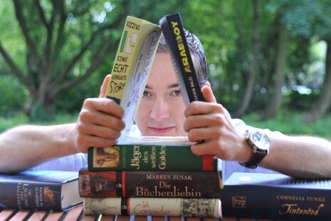 Підліток складає книжки одна на одну, як картковий будиночок