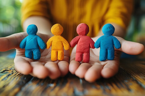 Des petites figurines en cire ou en pâte à modeler sont posées sur deux mains tendues.