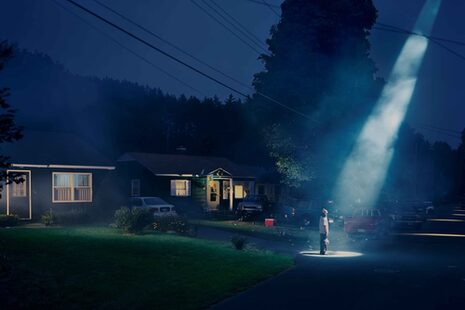 In der Nacht steht ein Mann vor seinem Haus in einem Lichtstrahl von oben
