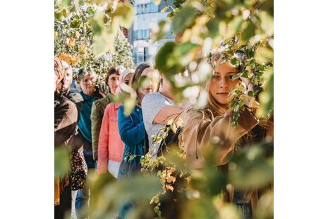 La photo montre une série de personnes en gros plan, debout au milieu d'arbres et en partie cachées par ceux-ci.